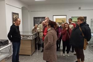 Pomieszczenie izby pamięci. Grupa osób slucha pana przewodnika
