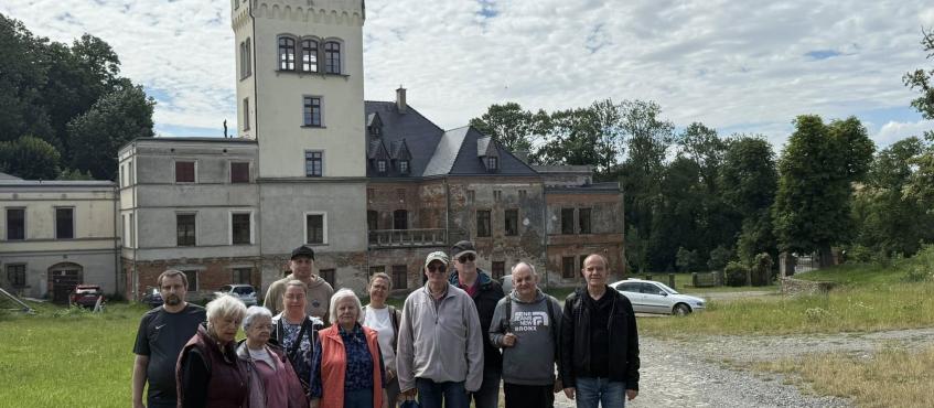 Na pierwszym planie stoi grupa osób, uczestników wycieczki. W tle znajduje się zamek