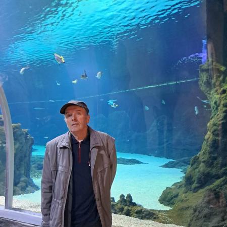 Wyświetl większy obrazek Mężczyzna w czapeczce pozuje w tunelu wodnym w Oceanarium. Za nim pływają ryby. 