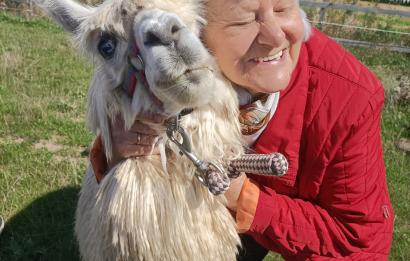 zdjęcie przedstawia uśmiechniętą kobietę, kobieta przytula alpakę