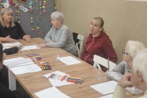Uczestnicy grupy wsparcia siedza przy wielkim stole. Przed sobą mają kartki